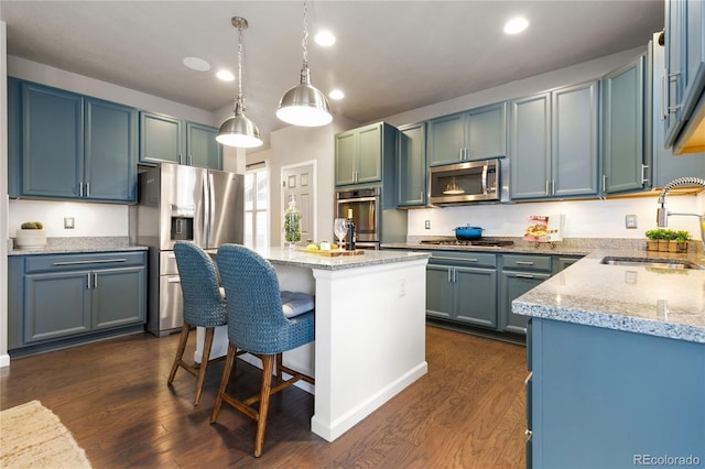 kitchen featuring light stone countertops, dark wood-type flooring, a sink, appliances with stainless steel finishes, and a center island