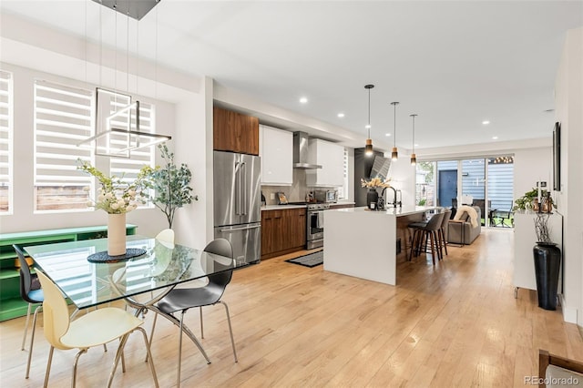 kitchen with appliances with stainless steel finishes, hanging light fixtures, a kitchen breakfast bar, wall chimney exhaust hood, and a kitchen island with sink