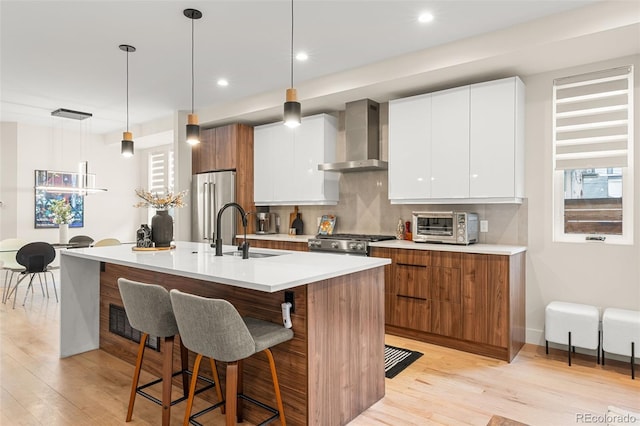 kitchen featuring wall chimney range hood, a center island with sink, white cabinetry, and sink