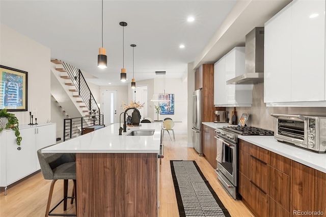 kitchen with a kitchen island with sink, hanging light fixtures, premium appliances, white cabinets, and wall chimney exhaust hood