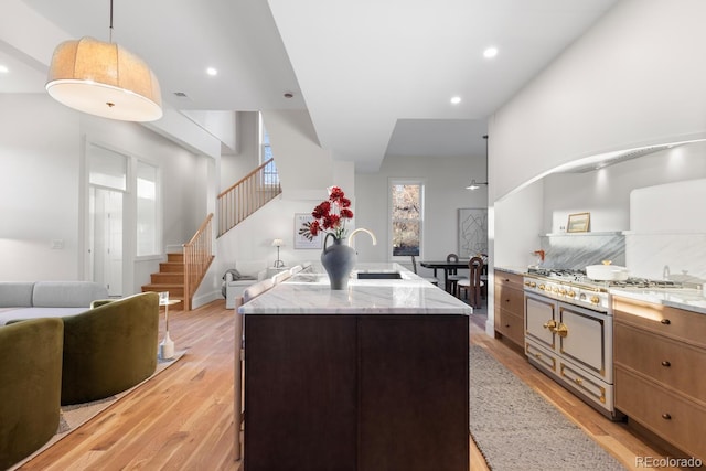 kitchen with a kitchen island, range with two ovens, light stone counters, and hanging light fixtures