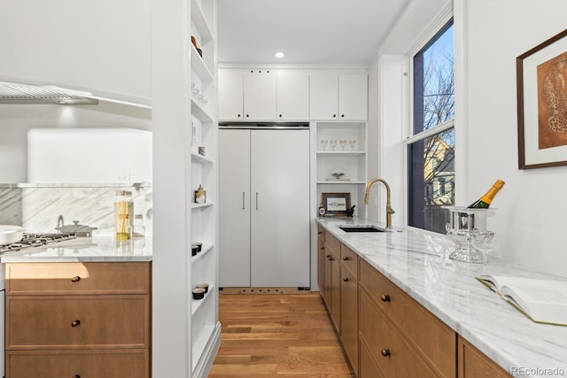 kitchen with light stone counters, a sink, white cabinets, light wood-type flooring, and open shelves