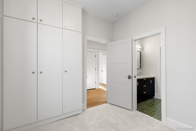 unfurnished bedroom featuring sink, ensuite bathroom, a closet, and light colored carpet