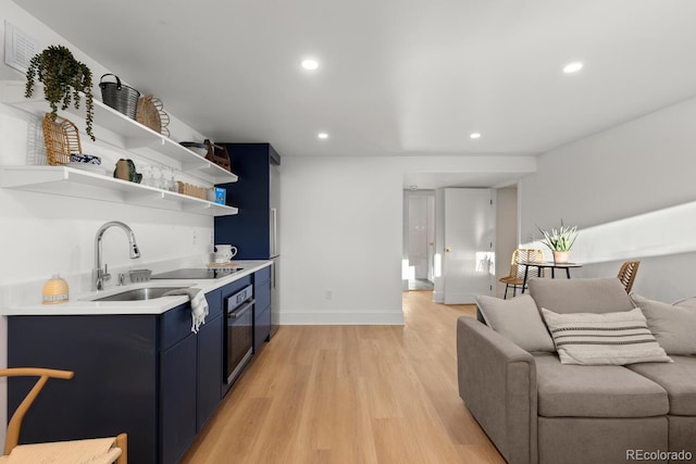 kitchen with black oven, blue cabinetry, light countertops, light wood-type flooring, and open shelves