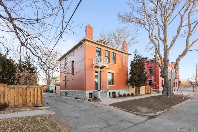 view of front of house featuring a balcony, brick siding, an outdoor structure, fence, and a chimney