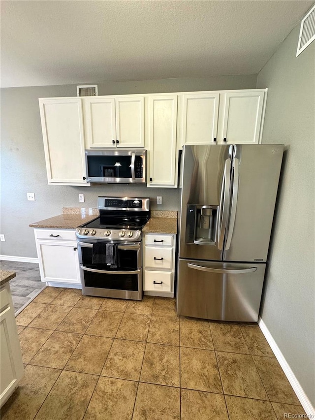 kitchen featuring stone counters, white cabinets, light tile patterned floors, a textured ceiling, and stainless steel appliances