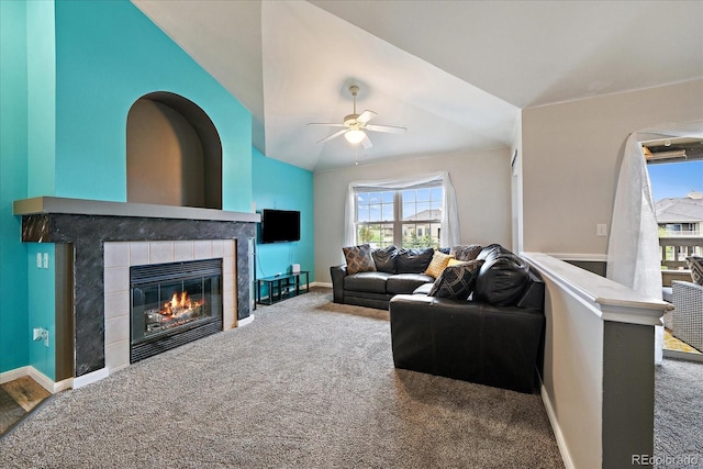 living room featuring vaulted ceiling, ceiling fan, carpet floors, a tiled fireplace, and baseboards