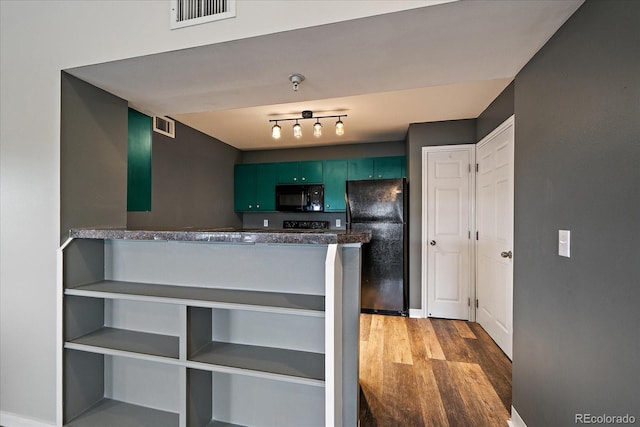 kitchen featuring black appliances, green cabinetry, wood finished floors, dark countertops, and a peninsula