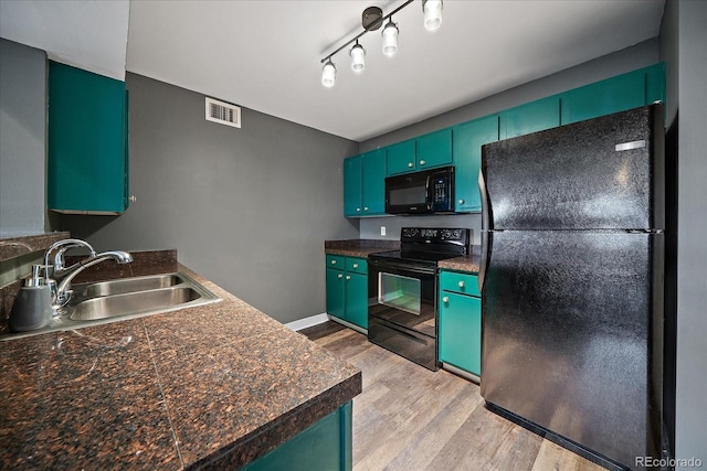 kitchen featuring black appliances, a sink, light wood finished floors, and dark countertops