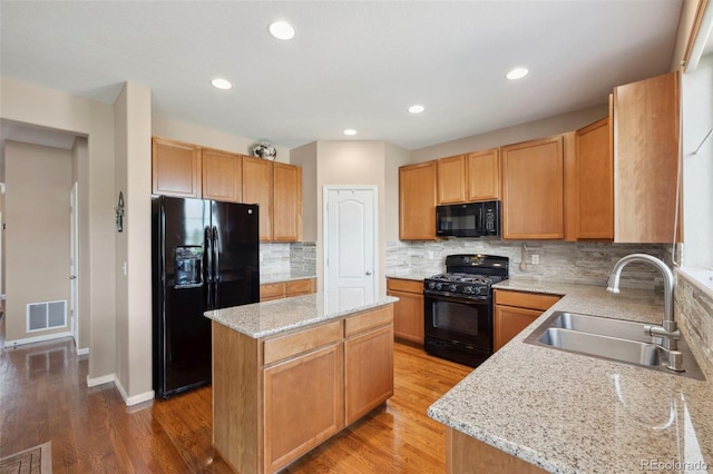 6612 Big Leaf Ln, Colorado Springs, CO 80927 - kitchen featuring black appliances, a center island, decorative backsplash, light stone counters, and light wood-style flooring