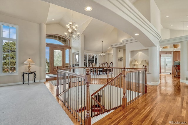 stairs with high vaulted ceiling, a notable chandelier, and wood-type flooring