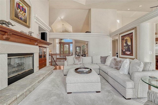 living room with a high ceiling, a stone fireplace, and light colored carpet