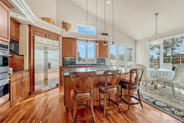 kitchen featuring stainless steel built in refrigerator, high vaulted ceiling, a kitchen island, light hardwood / wood-style flooring, and decorative light fixtures