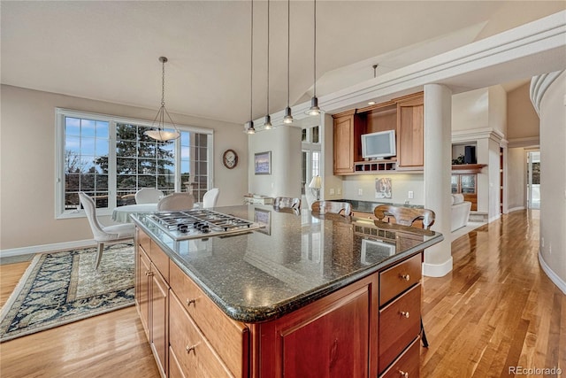 kitchen with light hardwood / wood-style floors, stainless steel gas cooktop, dark stone counters, hanging light fixtures, and a kitchen island