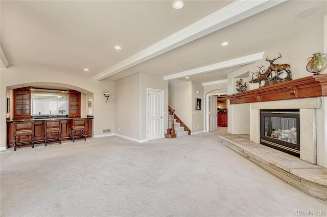 living room featuring a stone fireplace, ornamental molding, and carpet