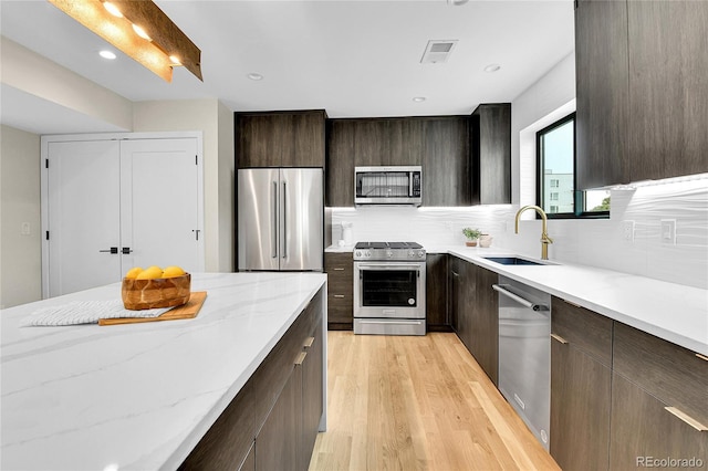 2162 S Ash St, Denver, CO 80222 - kitchen with stainless steel appliances, a sink, light wood-style flooring, decorative backsplash, and dark brown cabinets