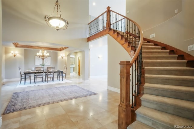 foyer entrance featuring stairway, arched walkways, a towering ceiling, and baseboards