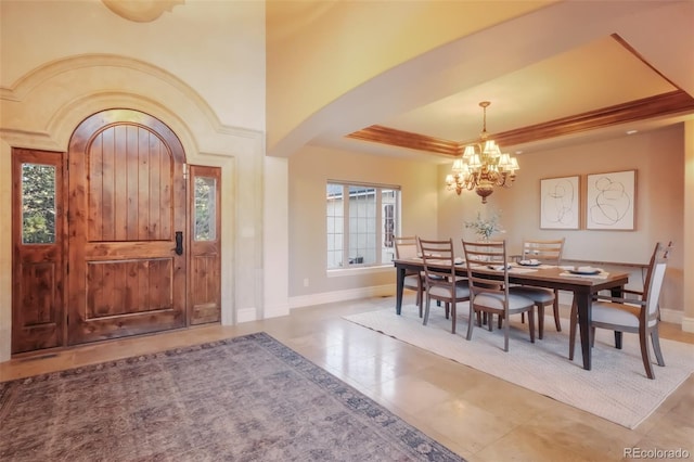 foyer entrance with baseboards, arched walkways, a raised ceiling, and an inviting chandelier