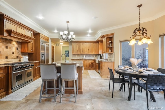 kitchen featuring premium appliances, crown molding, a notable chandelier, a center island with sink, and open shelves