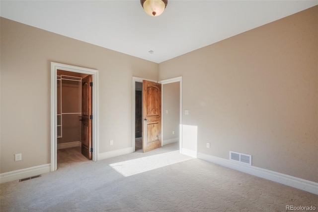 unfurnished bedroom with light carpet, a spacious closet, visible vents, and baseboards