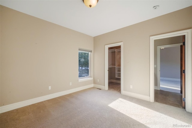 unfurnished bedroom featuring carpet, a spacious closet, baseboards, and a closet