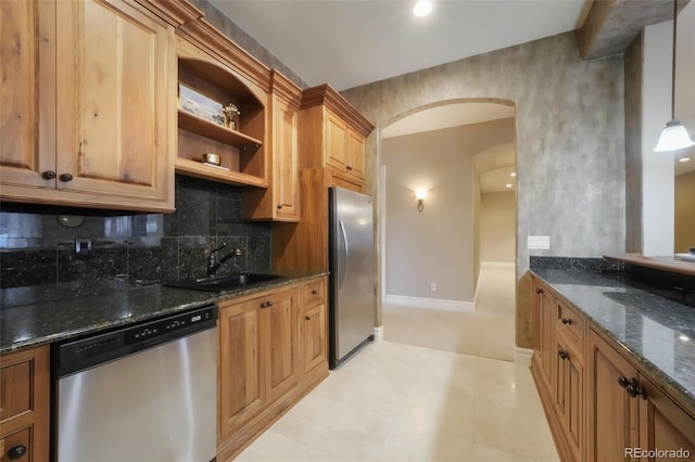 kitchen featuring arched walkways, stainless steel appliances, a sink, tasteful backsplash, and dark stone countertops