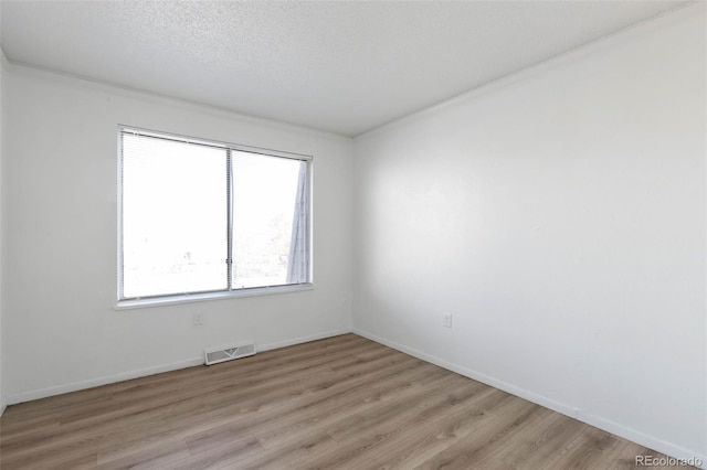 unfurnished room with light hardwood / wood-style floors, a textured ceiling, and ornamental molding