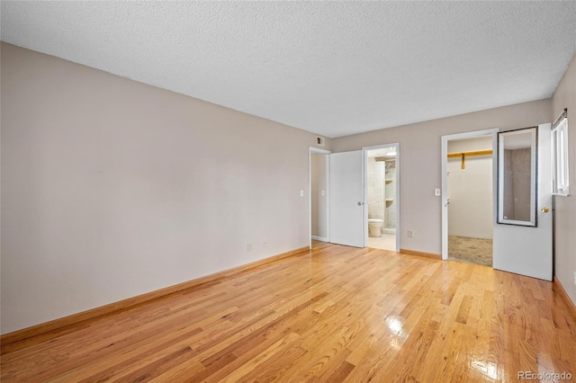 unfurnished bedroom with a walk in closet, ensuite bathroom, light hardwood / wood-style flooring, and a textured ceiling