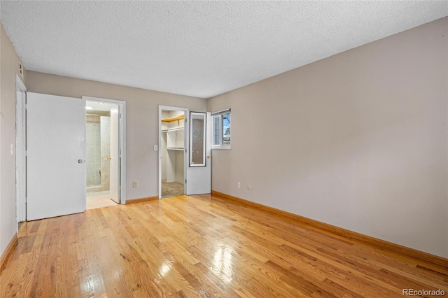 unfurnished bedroom featuring connected bathroom, a walk in closet, light hardwood / wood-style flooring, and a textured ceiling