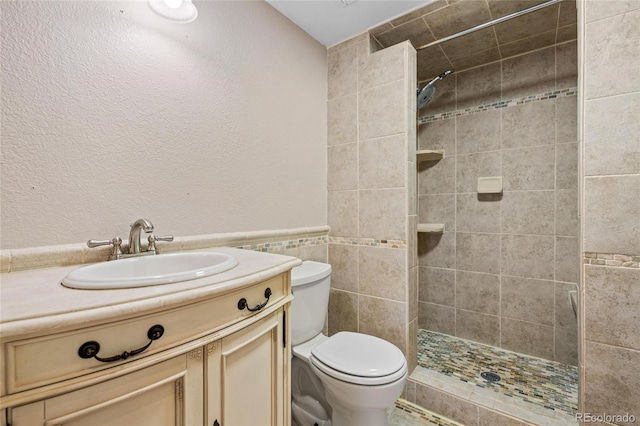 bathroom featuring vanity, toilet, tiled shower, and tile walls