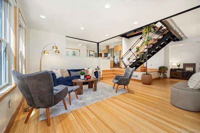 living room featuring baseboards, a healthy amount of sunlight, stairs, and light wood finished floors