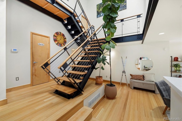 stairs with baseboards, wood finished floors, visible vents, and a high ceiling