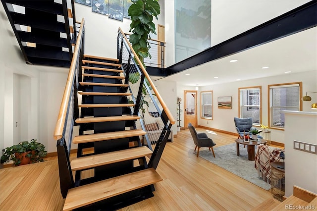 staircase with recessed lighting, wood finished floors, a high ceiling, and baseboards