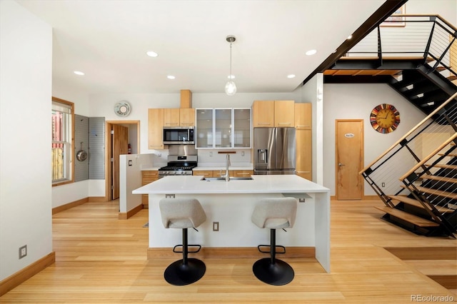 kitchen with light countertops, a sink, light wood-type flooring, baseboards, and appliances with stainless steel finishes