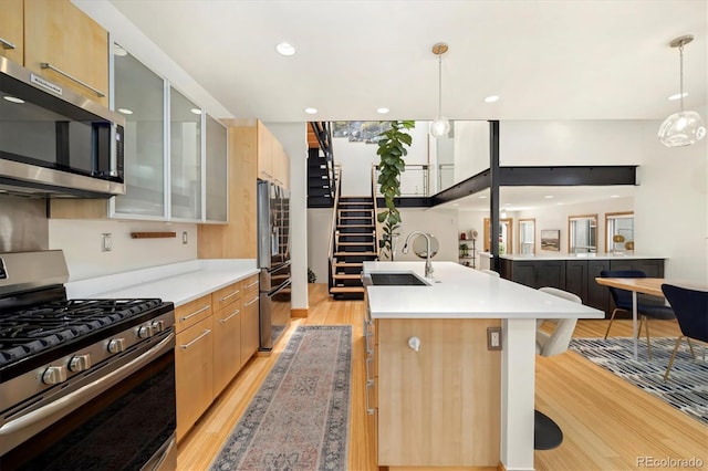 kitchen featuring an island with sink, stainless steel appliances, light countertops, a sink, and light wood-style flooring