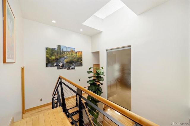 hallway with recessed lighting, light wood-type flooring, a skylight, and an upstairs landing