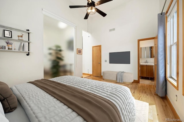 bedroom with a sink, connected bathroom, light wood-type flooring, a towering ceiling, and visible vents