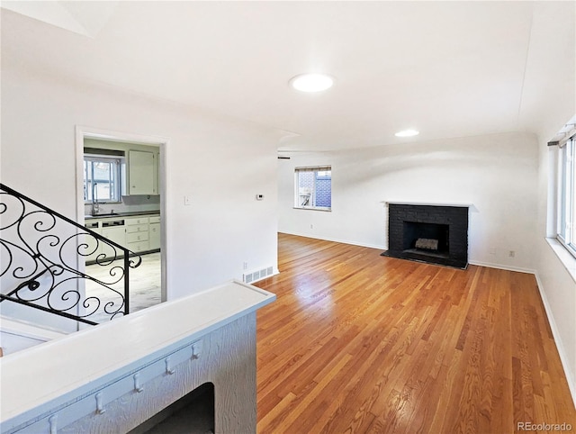 unfurnished living room with light wood finished floors, a sink, baseboards, visible vents, and a brick fireplace