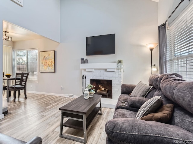 living area with visible vents, baseboards, a high ceiling, light wood-type flooring, and a brick fireplace