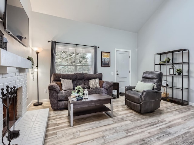 living room featuring light wood-style floors, baseboards, a fireplace, and high vaulted ceiling