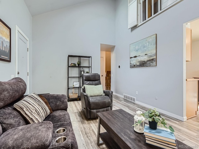 living area with light wood finished floors, a high ceiling, visible vents, and baseboards