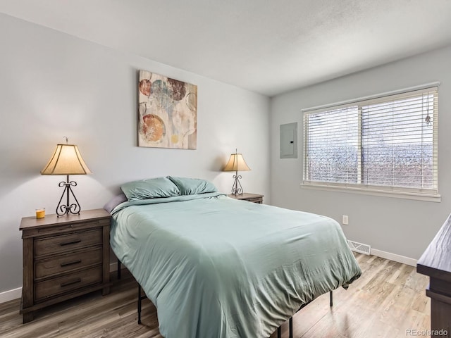 bedroom featuring light wood-style floors, electric panel, visible vents, and baseboards