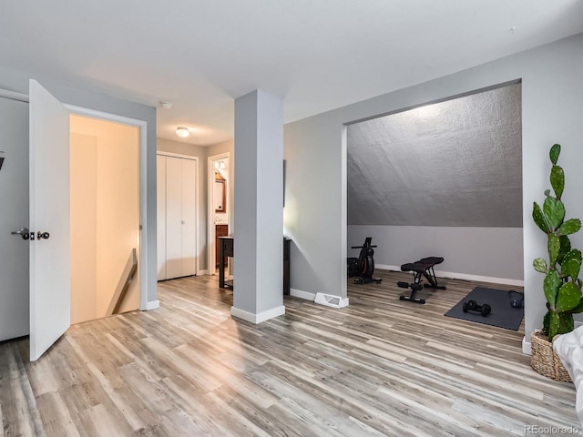 exercise area featuring lofted ceiling, light wood finished floors, and baseboards