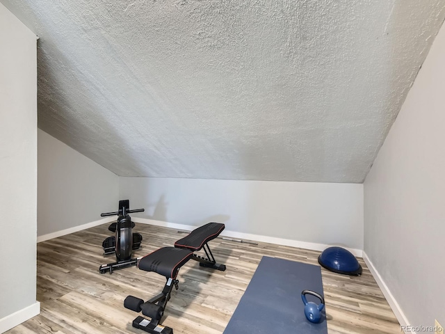 exercise room with lofted ceiling, a textured ceiling, baseboards, and wood finished floors