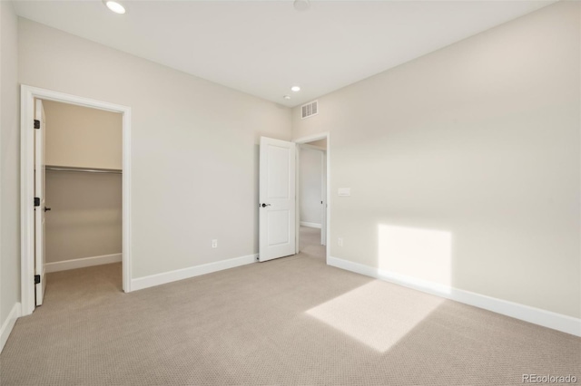 unfurnished bedroom featuring a spacious closet, a closet, and light colored carpet