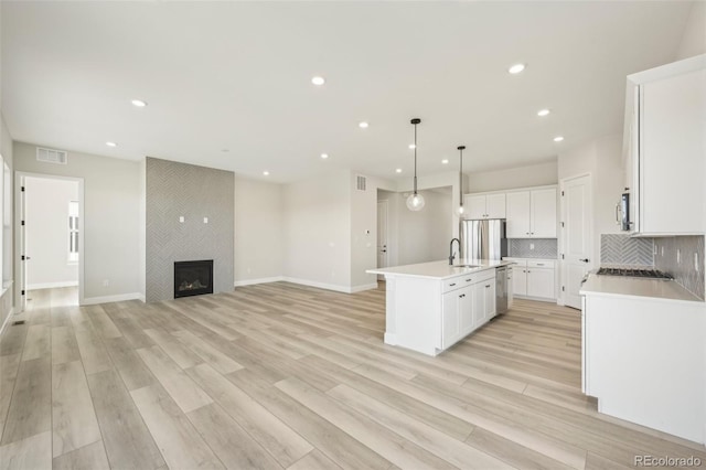 kitchen with hanging light fixtures, a center island with sink, a large fireplace, white cabinets, and backsplash