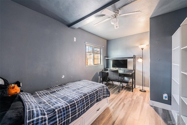 bedroom with ceiling fan, beamed ceiling, a textured ceiling, and light wood-type flooring