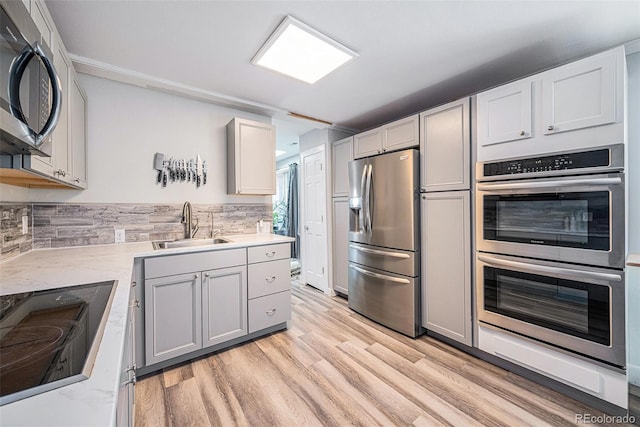 kitchen with decorative backsplash, light stone countertops, stainless steel appliances, sink, and light hardwood / wood-style floors