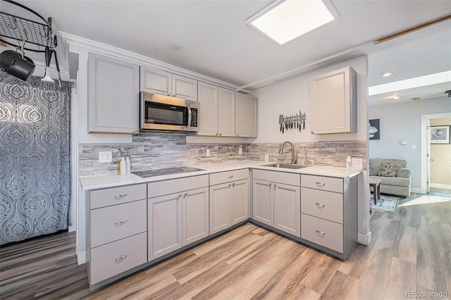 kitchen with black electric stovetop, backsplash, sink, light hardwood / wood-style flooring, and gray cabinets