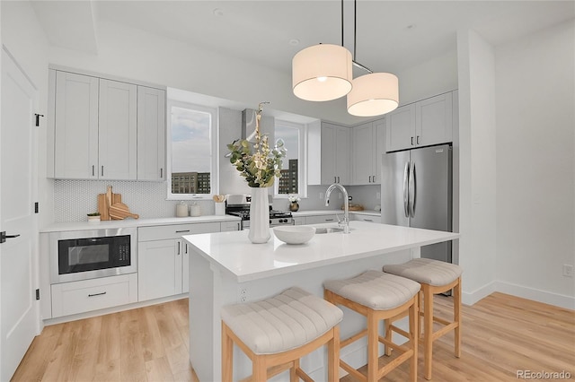 kitchen featuring sink, decorative light fixtures, an island with sink, stainless steel appliances, and decorative backsplash